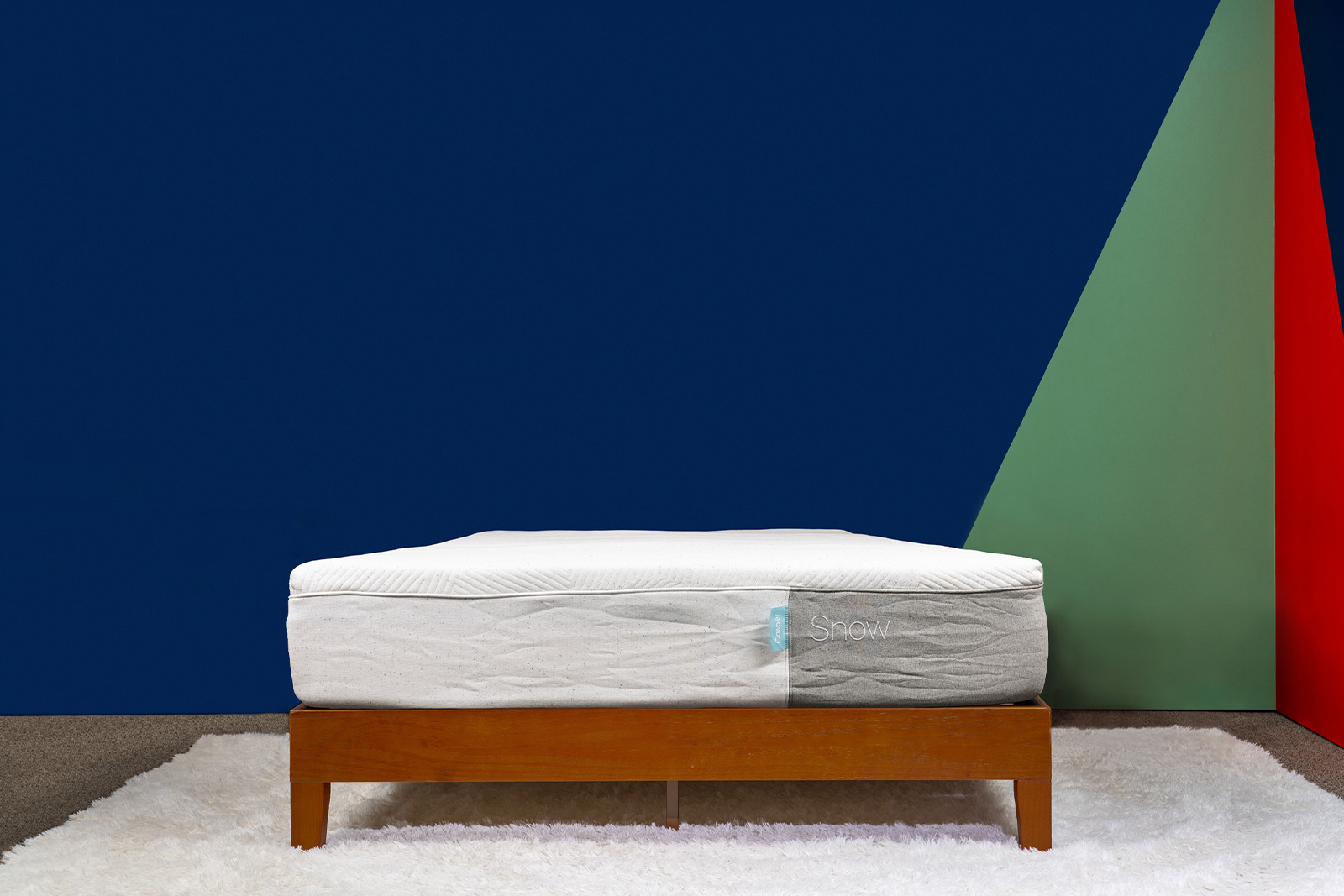 Distant photo of the Casper Snow Mattress on a bedframe in a bedroom taken from a front angle.
