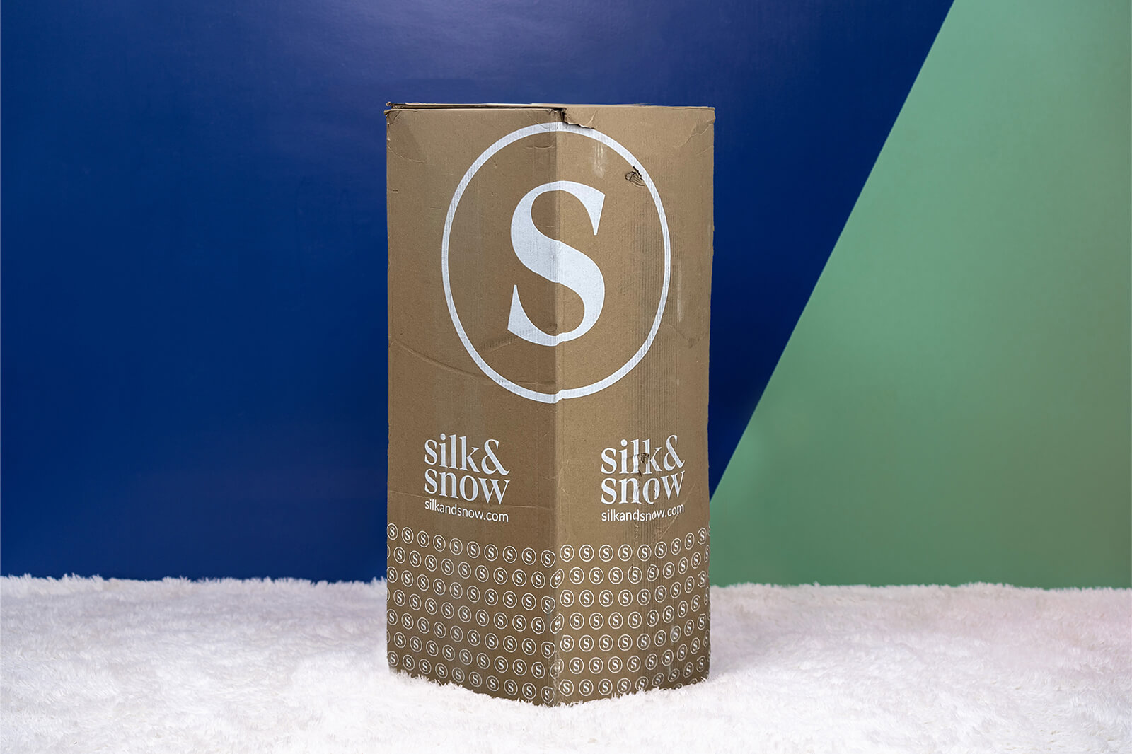 Photo of the Silk and Snow Organic Mattress box on the floor in a bedroom taken from a front angle.