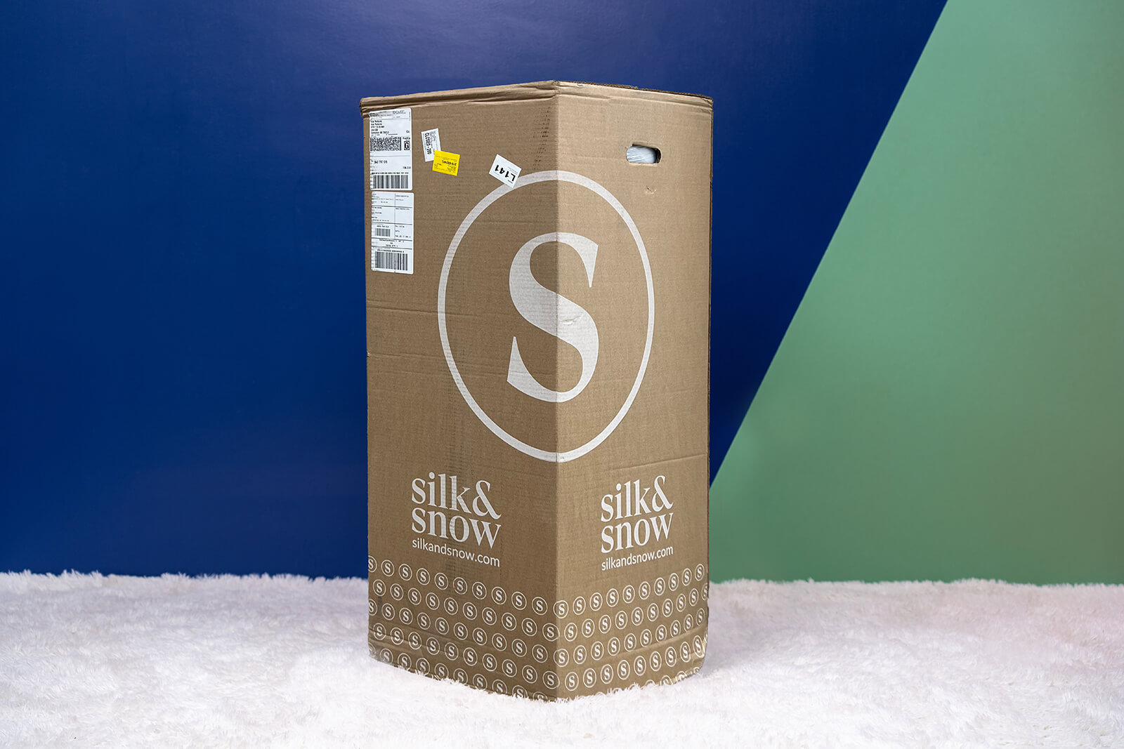 Photo of the Silk & Snow Mattress box on the floor in a bedroom taken from a front angle.